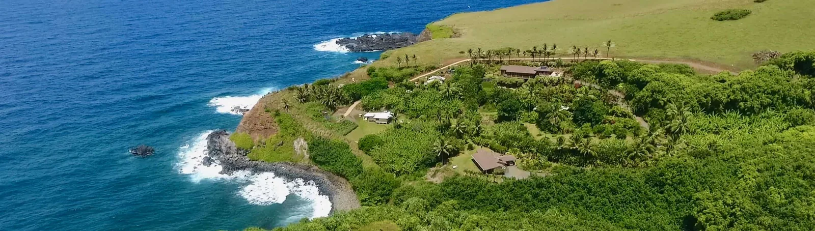 Lush green North Shore coastline near Ha'iku with blue ocean, black lava cliffs and a tropical estate