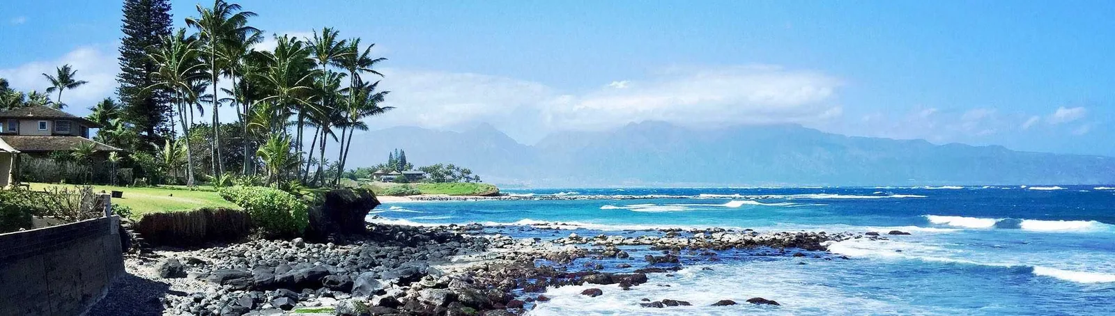 Rocky Pa'ia shoreline with palms, turquoise reef water and the West Maui mountains in the distance